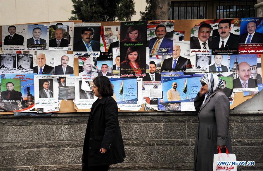  Two Syrian women walk by the posters of candidates for Syria