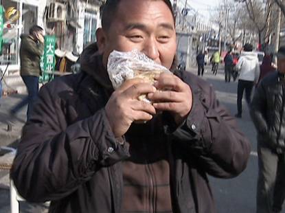 求职者樊小兵拿着刚刚买的大饼在胡同里吃了起来
